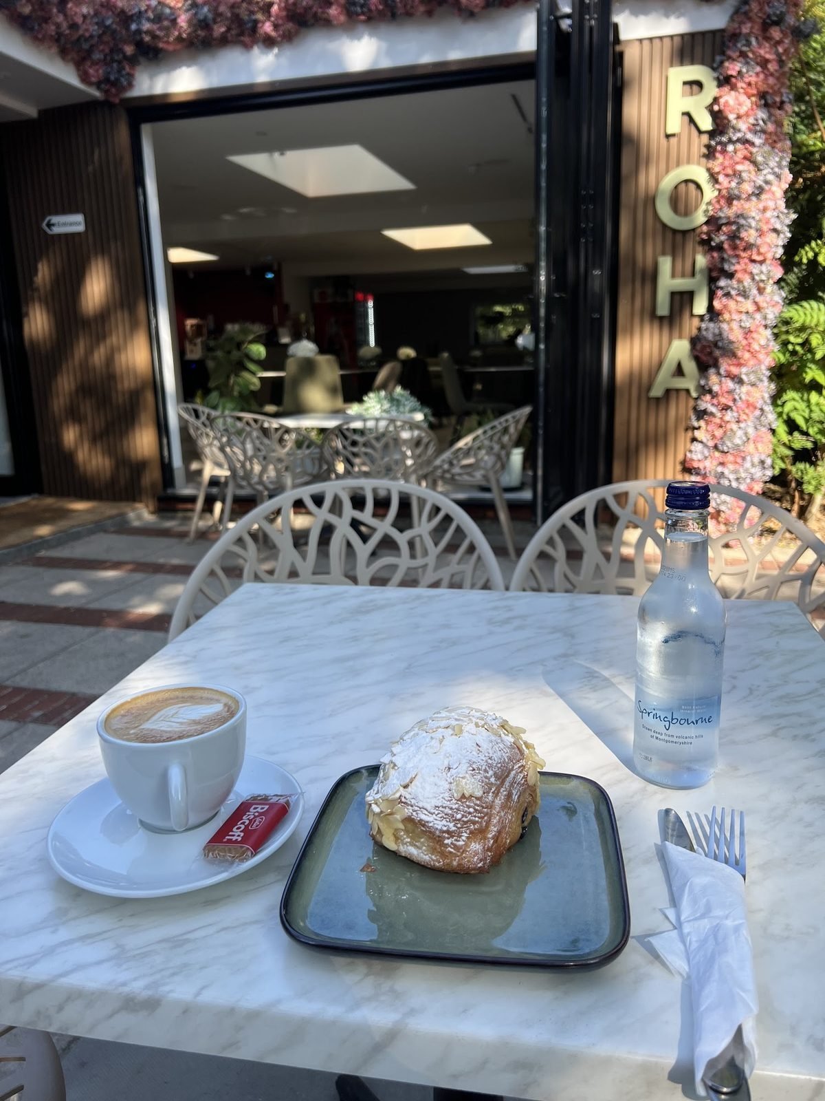 Coffee and an almond pastry on a marble table outside ROHA Cafe